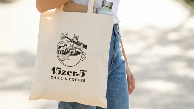 Modella in jeans e t-shirt bianca indossa una tote bag in cotone 15zero5 chill e coffee. Sulla tote bag è raffigurato un bradipo immerso in una tazza di caffè.